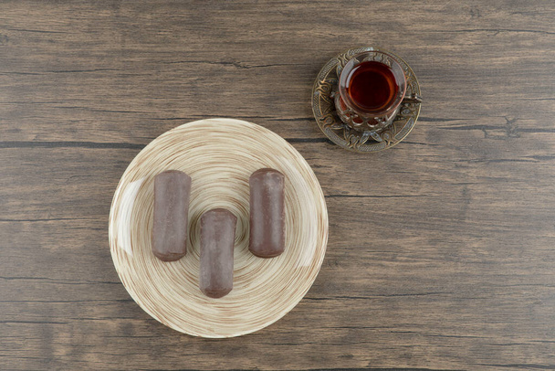 Plate of chocolate cake bar with glass of tea on wooden surface. High quality photo - Photo, image