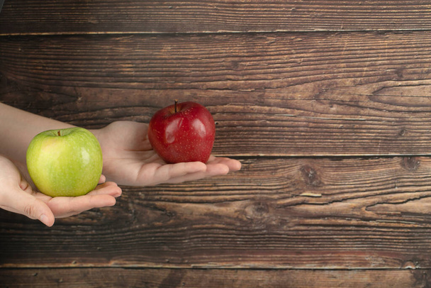 Ženské ruce drží červené jablko a zelené jablko na dřevěném pozadí. Kvalitní fotografie - Fotografie, Obrázek