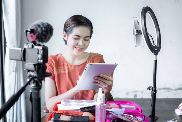 Asian beautiful fashion beauty blogger looks into a digital camera. reviews beauty product for video blog,  talking on cosmetics holding a makeup palette while recording her video. - Photo, Image