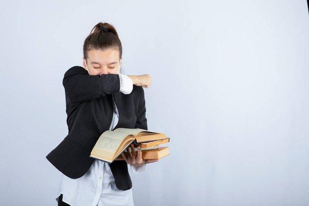 Młoda studentka trzymająca książki i zakrywająca usta nad białą ścianą. Wysokiej jakości zdjęcie - Zdjęcie, obraz