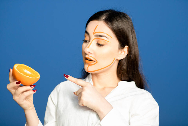 Foto de mulher bonita com rosto pintado apontando para metade da fruta laranja. Foto de alta qualidade - Foto, Imagem