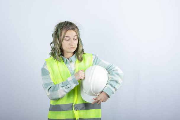 白い背景に硬い帽子を保持緑のベストで若い建設労働者の写真。高品質の写真 - 写真・画像