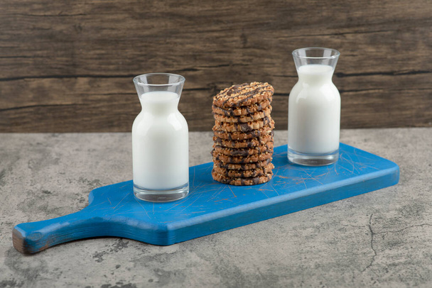 Two glass jugs of milk with oatmeal cookies on a blue wooden board. High quality photo - Photo, Image