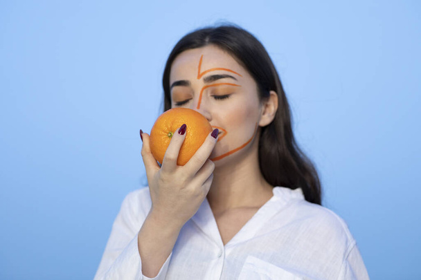 Προσωπογραφία νεαρής γυναίκας με ζωγραφισμένο πρόσωπο που κρατάει ένα πορτοκάλι. Υψηλής ποιότητας φωτογραφία - Φωτογραφία, εικόνα