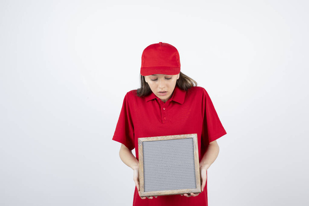 Immagine di giovane ragazza adolescente in uniforme rossa in piedi e con cornice in mano. Foto di alta qualità - Foto, immagini