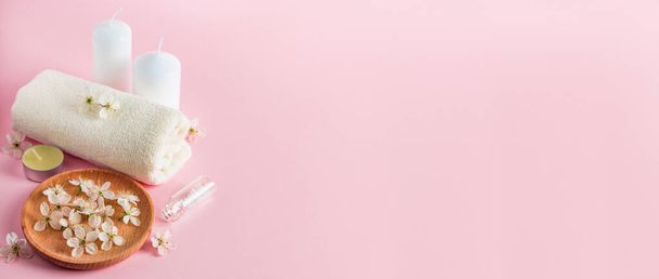 Cosmetic products for spa and aromatherapy. Candles, sea salt, towel and flowers on a pink background. Skin care and beauty concept. Place for your text, banner format - Foto, imagen