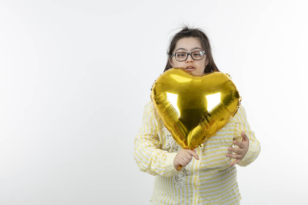 Portrait of young girl with a Down syndrome holding air balloon in shaped of heart . High quality photo - Photo, Image