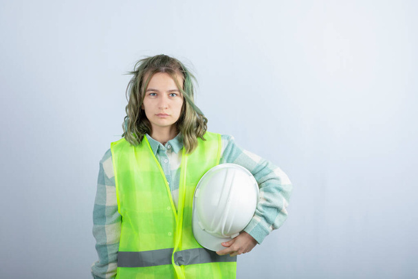白い背景に硬い帽子を保持緑のベストで若い建設労働者の写真。高品質の写真 - 写真・画像