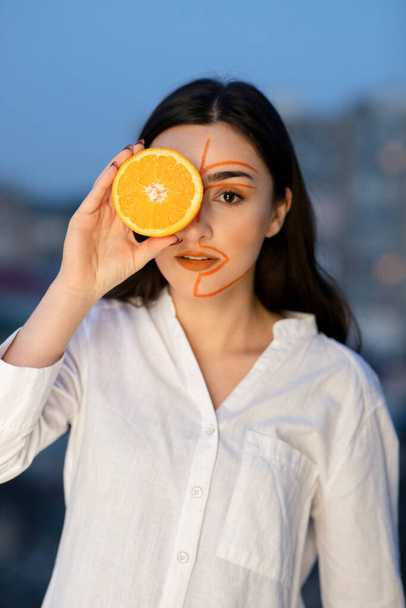 Foto di bella donna con viso dipinto che copre l'occhio con metà di frutta arancione. Foto di alta qualità - Foto, immagini