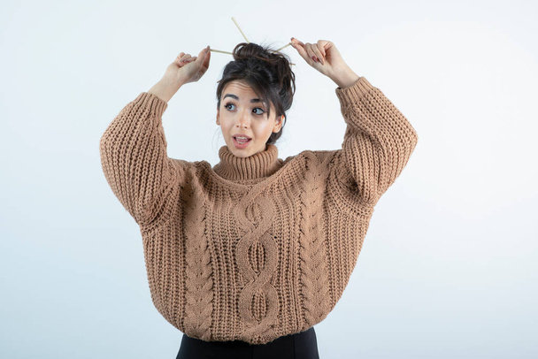 Portrait de jeune belle femme en tricot faisant ses cheveux avec des stylos. Photo de haute qualité - Photo, image
