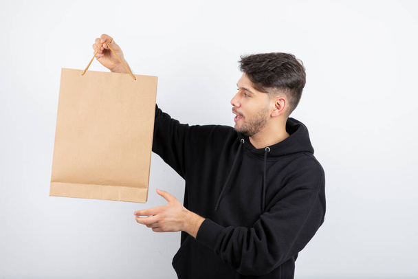 Foto de un hombre guapo con capucha negra mostrando una bolsa de artesanía. Foto de alta calidad - Foto, imagen