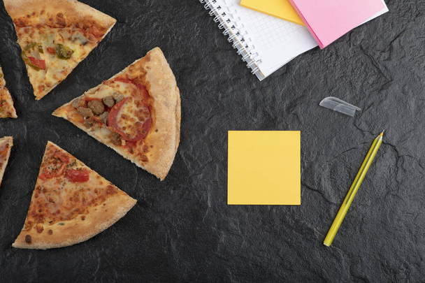 Rodajas de pizza de pepperoni picante y almohadillas de notas en la superficie negra. Foto de alta calidad - Foto, Imagen