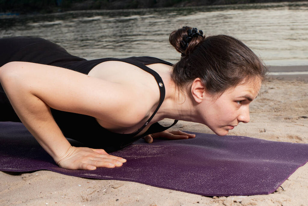 Una donna si trova in una posa tavola sulla riva del fiume sulla spiaggia al tramonto in estate. Lezioni di yoga o fitness in natura. - Foto, immagini