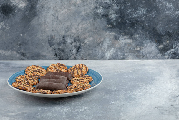 Mavi tabak dolusu çikolatalı kek ve mermer yüzeyde kepekli kurabiye. Yüksek kalite fotoğraf - Fotoğraf, Görsel