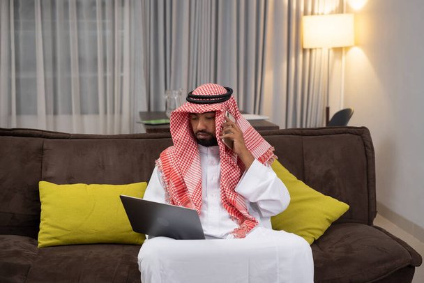 Arab businessman in a turban working using a laptop and making phone calls while sitting - Foto, afbeelding