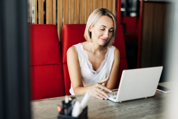 Una hermosa chica rubia usa un portátil y trabaja en un café. Romper, trabajar en línea, freelance - Foto, imagen