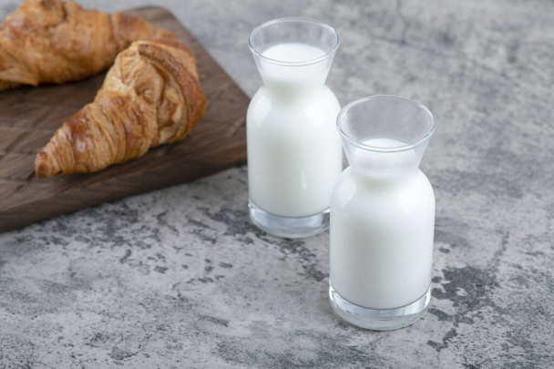 Croissants frescos y sabrosos con una jarra de vidrio de leche colocada sobre una mesa de piedra. Foto de alta calidad - Foto, Imagen