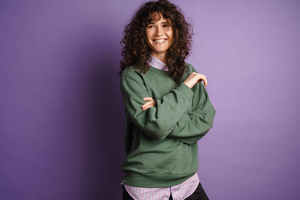 Happy beautiful curly girl smiling and looking at camera isolated over purple background - Photo, Image