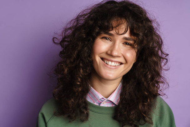Happy beautiful curly girl smiling and looking at camera isolated over purple background - Foto, Bild