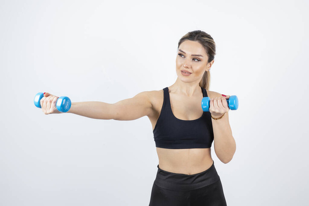 Blonde fit woman in black top standing and exercising with dumbbells . High quality photo - Foto, Bild