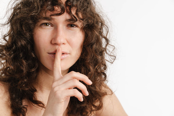 Half-naked curly woman posing and showing silence gesture isolated over white background - Foto, imagen