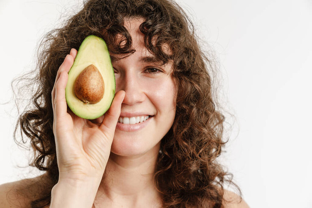 Half-naked curly woman smiling while posing with avocado isolated over white background - Foto, Imagem