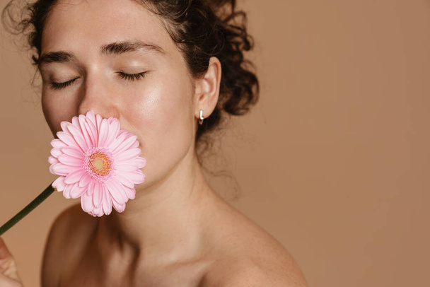 Half-naked european woman posing with pink flower isolated over beige background - Foto, Bild