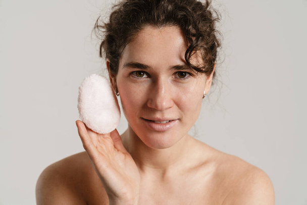 Half-naked curly woman posing with powder sponge isolated over white background - 写真・画像