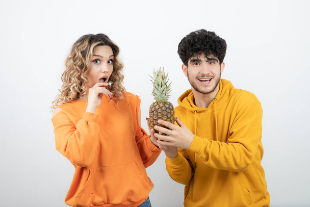 Jeune couple d'amis debout avec l'ananas contre le mur blanc. Photo de haute qualité - Photo, image