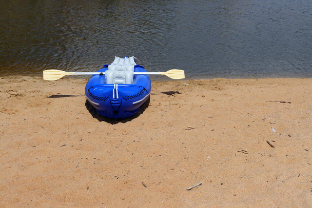 Голубая резиновая лодка и весла на песчаном берегу реки. надувная лодка - Фото, изображение