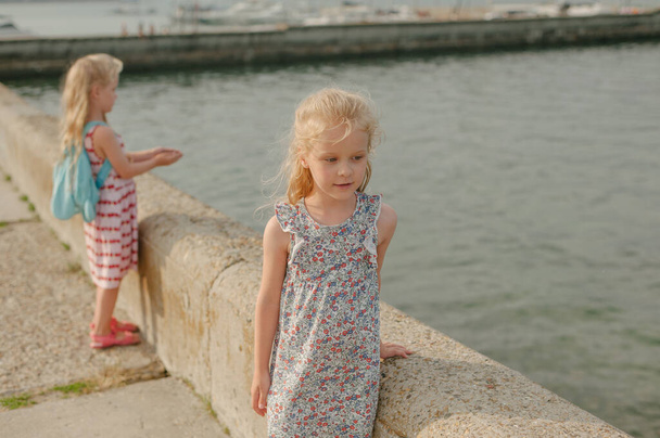 zwei kleine Mädchen mit langen weißen Haaren im Kleid schauen im Sommer auf der Seebrücke in die Ferne - Foto, Bild