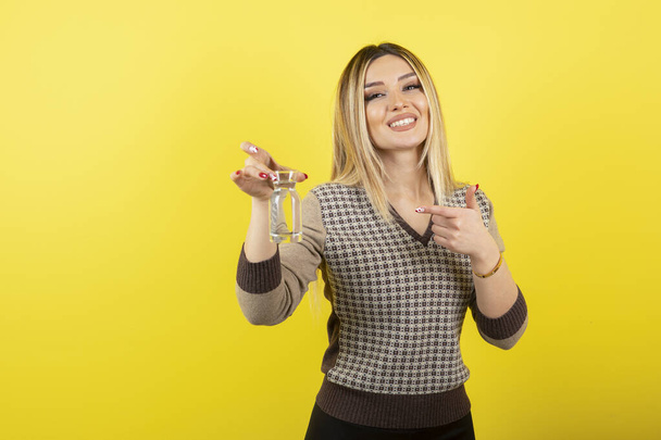 Portrait of blonde woman with glass of water standing over yellow. High quality photo - Valokuva, kuva