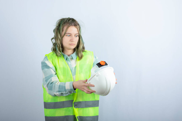 Foto de un joven trabajador de la construcción en chaleco verde que sostiene el sombrero sobre fondo blanco. Foto de alta calidad - Foto, Imagen