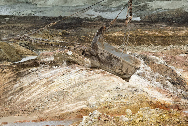 una excavadora grande carga una roca con un cubo con un camión volquete que extrae hierro o bauxita, en una cantera sobre el fondo del cubo del cielo - Foto, Imagen