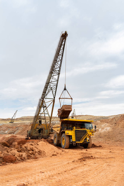 gran excavadora carga roca con hierro o bauxita camión volquete minero en una cantera contra el cielo - Foto, imagen