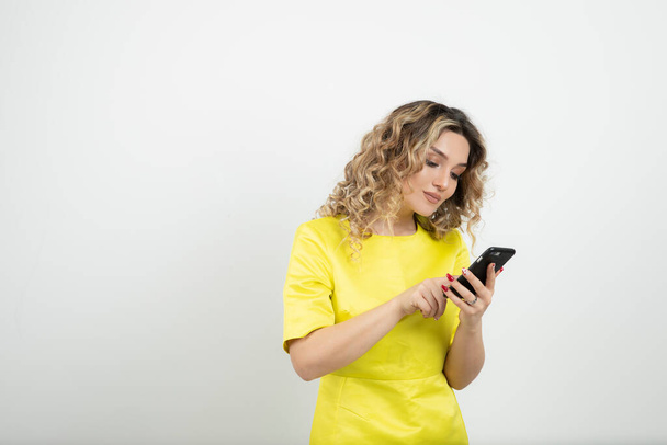 Photo of curly haired blonde woman in yellow dress checking her cellphone. High quality photo - Zdjęcie, obraz
