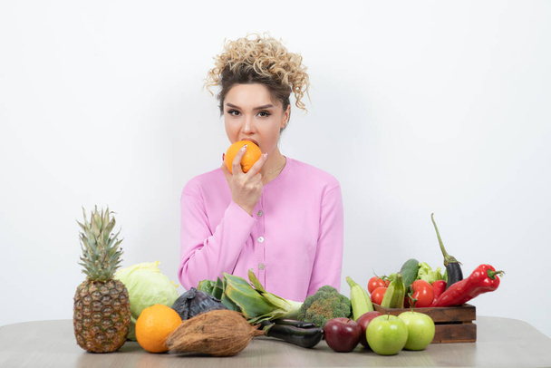 Curly woman sitting at table with a lot of various fresh vegetables - Photo, Image