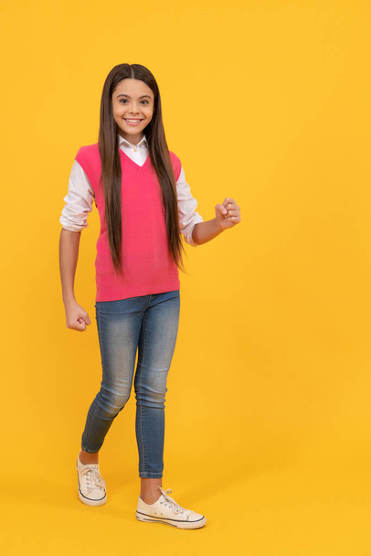 happy teen school girl walking on yellow background, copy space, fashion - Photo, Image
