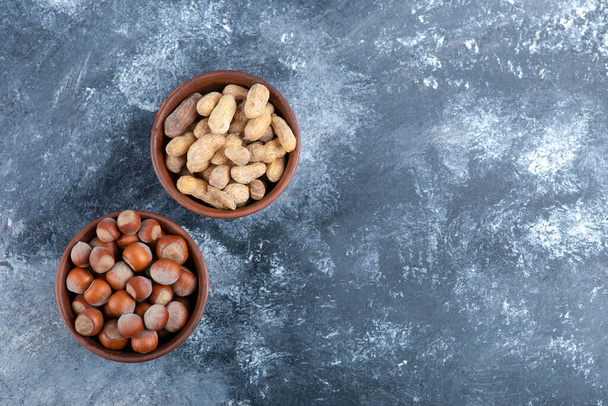 Kaksi kulhoa orgaanisia kuorittuja maapähkinöitä ja hasselpähkinöitä marmorilla. Laadukas kuva - Valokuva, kuva