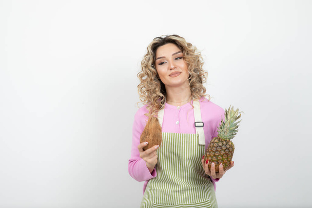 Beautiful curly woman in apron holding tropical fruits over white. High quality photo - Foto, Imagen