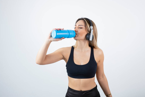 Красивая спортивная женщина в наушниках пьет из бутылки с водой. Высокое качество фото - Фото, изображение