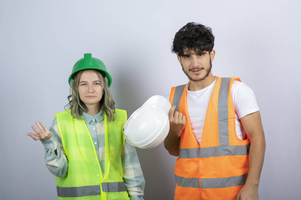 Dois jovens engenheiros femininos e masculinos em pé e posando sobre a parede branca. Foto de alta qualidade - Foto, Imagem