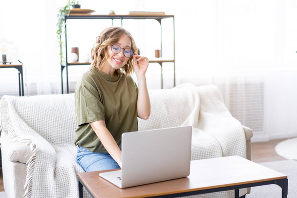 Woman with glasses use laptop typing keyboard sitting couch big window background home interior Freelance female working from home Distance learning student relaxing watch lessons video conferenc - Photo, image