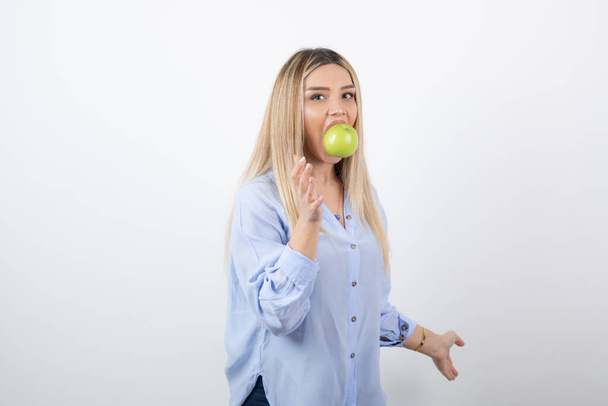Portrait photo of a pretty attractive woman model standing and eating a green fresh apple . High quality photo - Фото, зображення