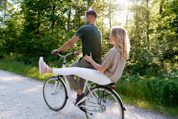 Vista posteriore della coppia che condivide una bicicletta nella foresta                                - Foto, immagini