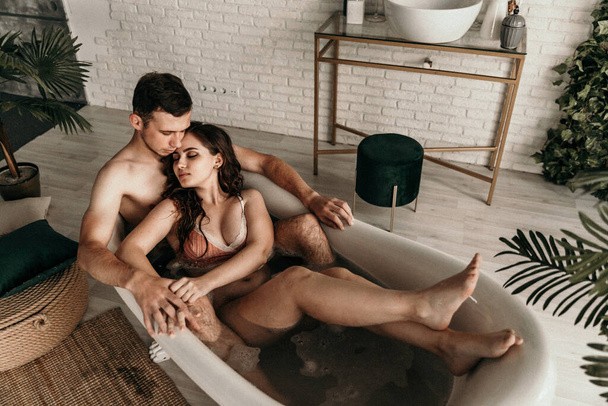 photo of young people in love taking a bath. mental rest. sexual instinct.carnal infatuation. handsome guy is feeling drawn toward his beautiful girlfriend. lovers joy in bathroom. noise, grainy effect - Foto, Bild