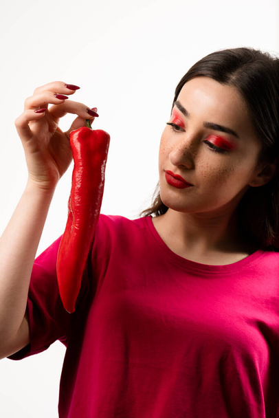 Image of brunette woman looking at red hot chili pepper in hand . High quality photo - Photo, Image