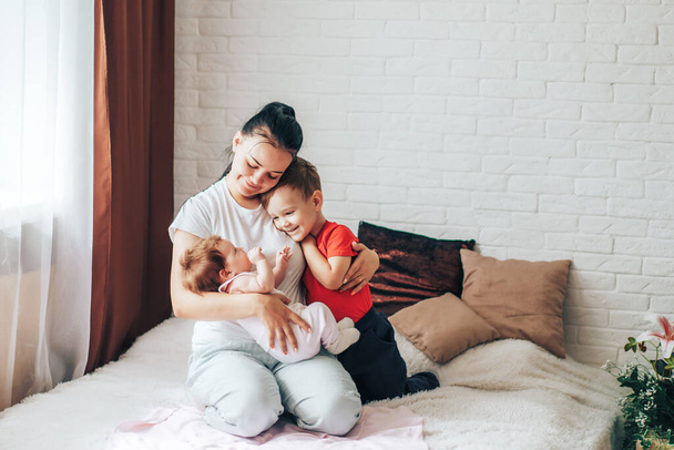 Молодая мать с двумя детьми играет на кровати. - Фото, изображение