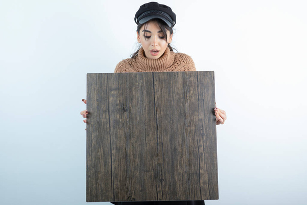 Mooie vrouw met zwarte pet, kijkend naar een stuk hout. Hoge kwaliteit foto - Foto, afbeelding