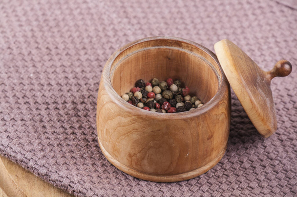 Wooden container with a lid for storing black pepper on the background of kitchen coasters and towels close up - Photo, image